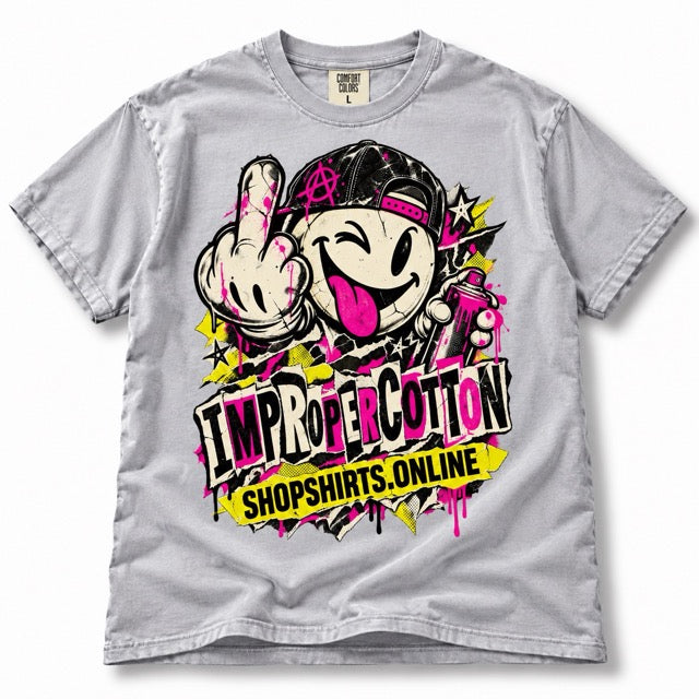 Light gray vintage wash Improper Cotton T-shirt featuring a bold graffiti-style winking smiley character with tongue out, middle finger, spray can, pink and yellow accents, and ShopShirts.online branding, displayed solo on a clean white background with a soft shadow.