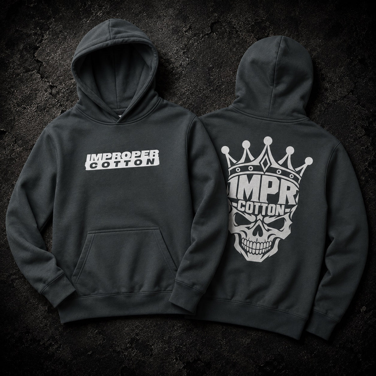Two dark charcoal gray hoodies shown from the front and back against a dark textured background. The front hoodie features a white 'IMPROPER COTTON' logo across the chest, and the back hoodie features a large white skull and crown graphic with the brand name.
