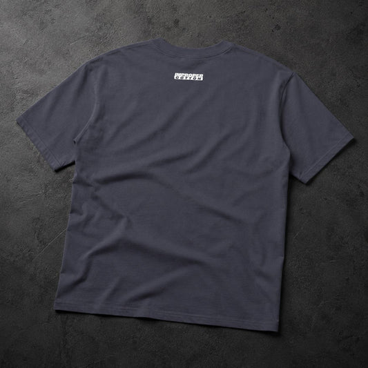 A dark charcoal gray t-shirt laid flat on a textured dark gray surface, featuring a small white rectangular graphic printed on the upper back.