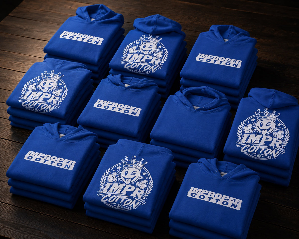 Nine folded royal blue hoodies are arranged in a grid on a dark wooden surface. Each hoodie features a white printed graphic with a crown, lightning bolt, and the words 'IMPROPER COTTON'.