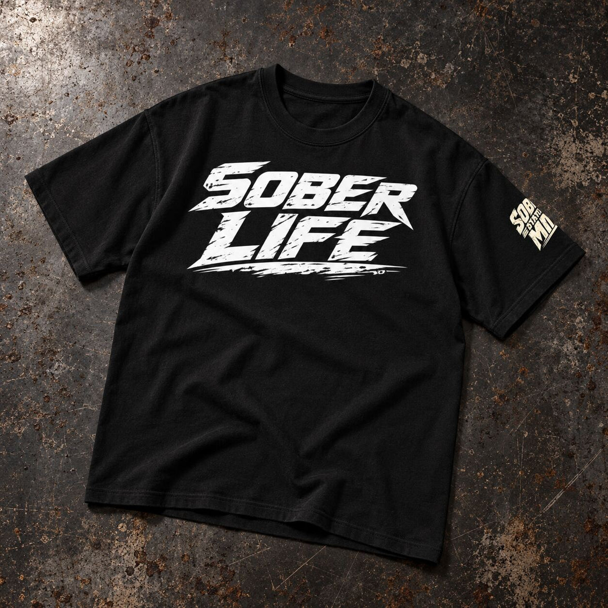 A black short-sleeve t-shirt with a distressed white 'SOBER LIFE' graphic on the chest and a small vertical white graphic on the right sleeve, laid flat on a textured dark gray and brown surface.