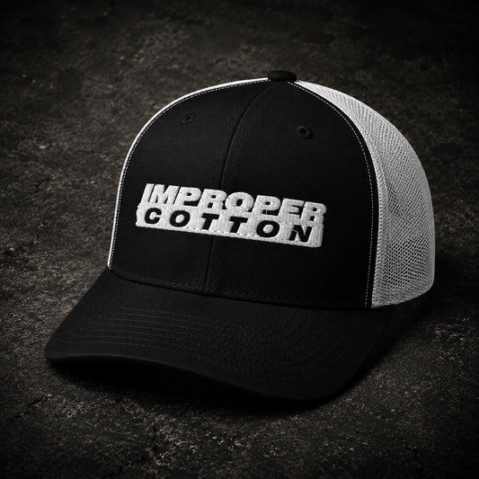 A black and white trucker hat with 'IMPROPER COTTON' embroidered on the front, set against a dark textured background.