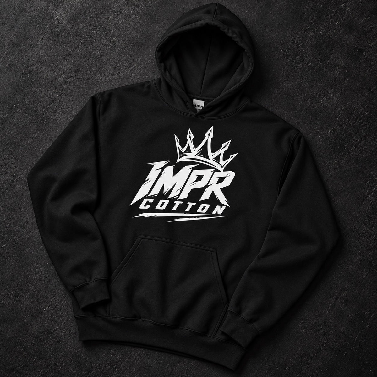 A black pullover hoodie laid flat on a dark textured background, featuring a large white graphic on the chest with a crown above stylized text reading 'IMPR COTTON'.