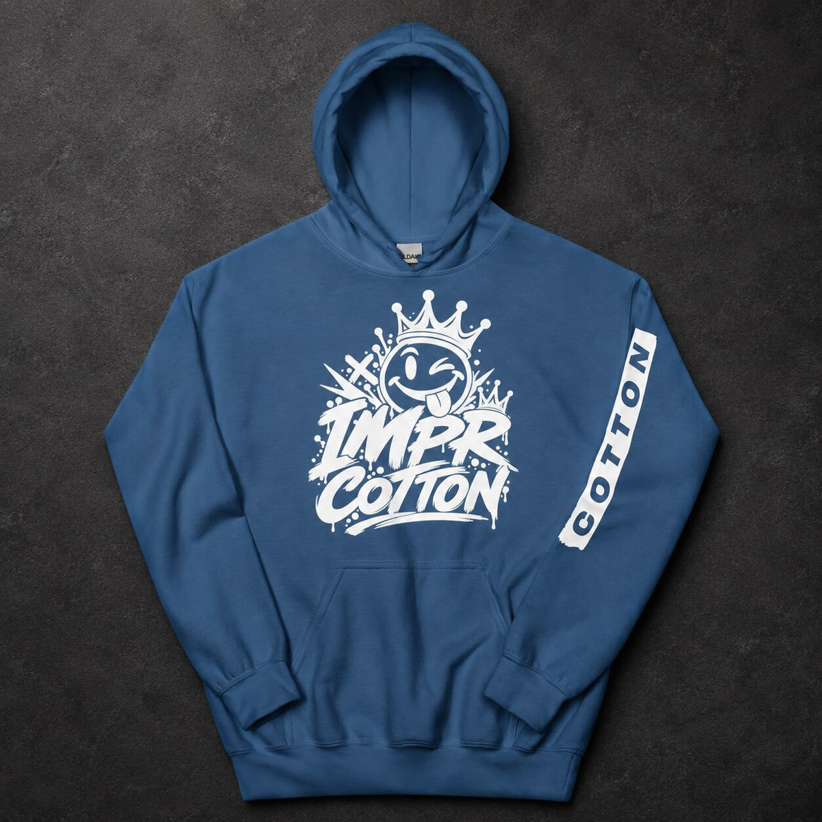 A blue pullover hoodie laid flat on a dark textured background, featuring a large white graphic on the chest with a crown and the words 'IMPR. COTTON,' plus a vertical white 'COTTON' label on the sleeve.