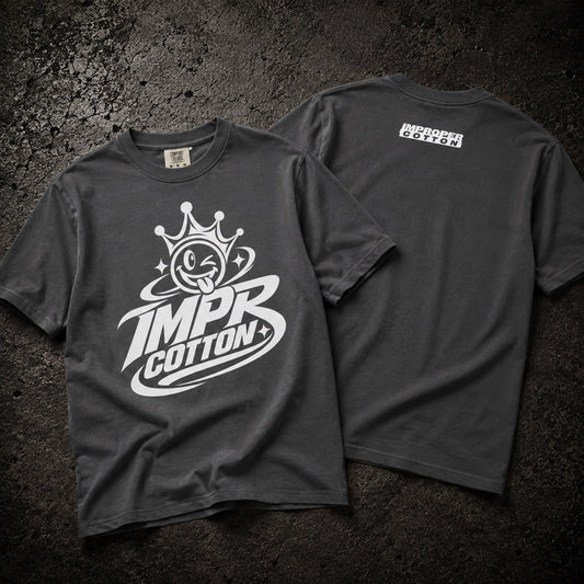 Two dark charcoal gray t-shirts displayed flat on a textured dark background, showing the front and back designs. The front features a large white graphic of a cartoon face inside a crown with the text 'IMPR COTTON+'.