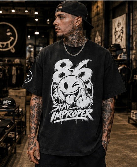 A man wearing a black graphic t-shirt with a white '86 Stay Improper' design, standing in a dimly lit clothing store.