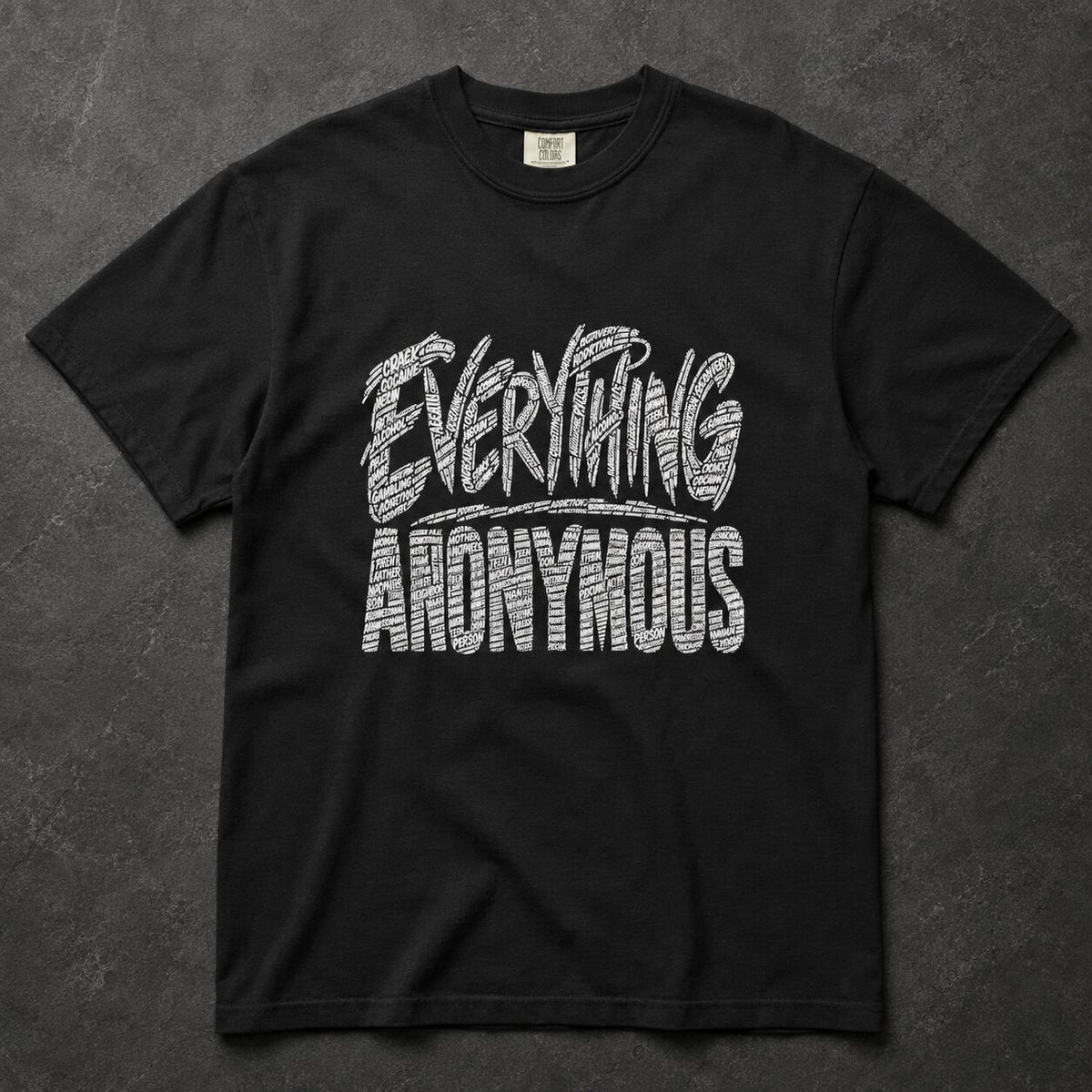 A black short-sleeve t-shirt with a white textured graphic reading 'EVERYTHING ANONYMOUS' across the chest, laid flat on a dark gray textured background.