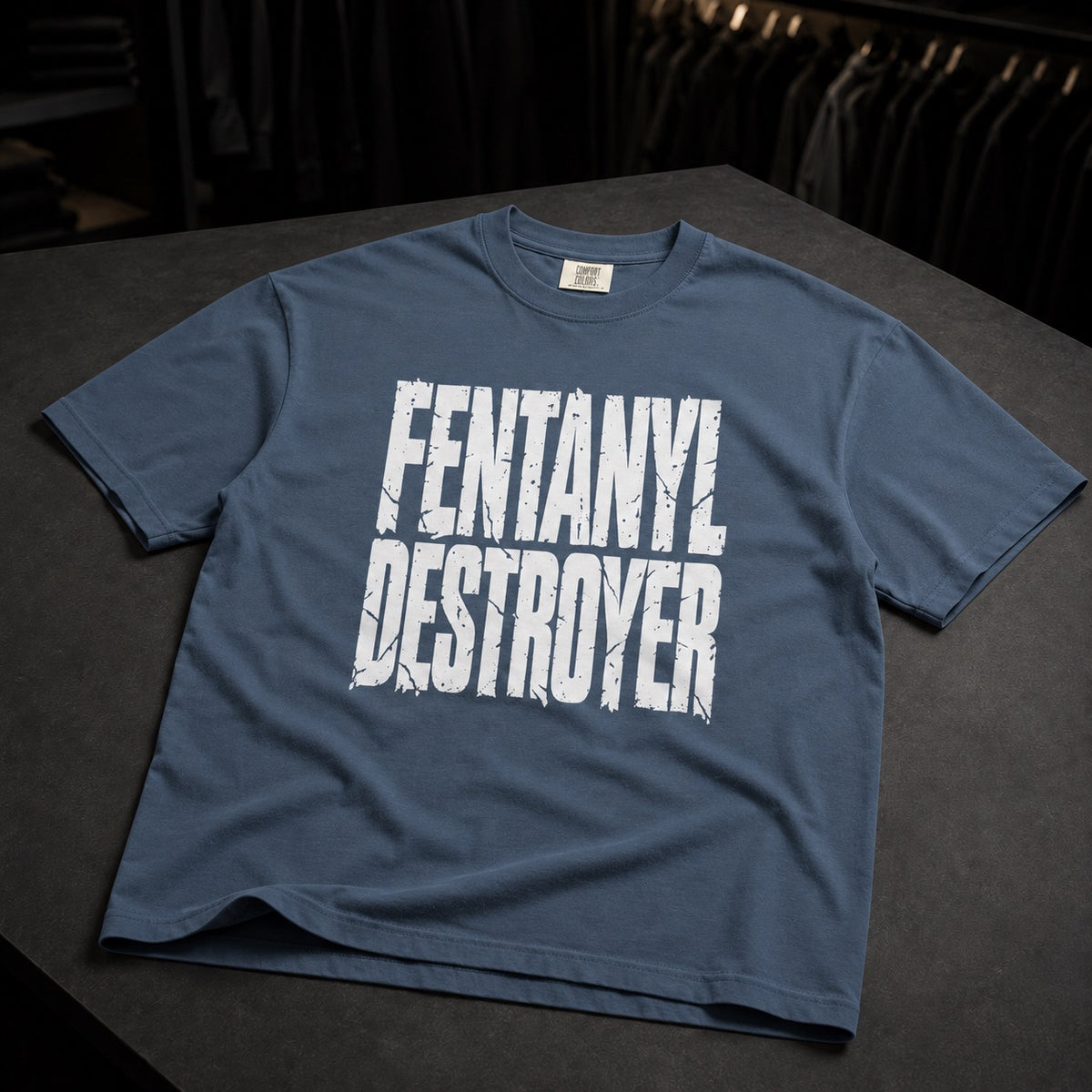 A slate blue short-sleeve t-shirt with a distressed white graphic reading 'FENTANYL DESTROYER' laid flat on a dark gray surface.