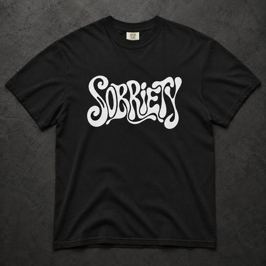A black short-sleeve t-shirt with the word 'SOBRIETY' printed across the chest in a stylized white bubble-letter font, laid flat on a dark textured background.