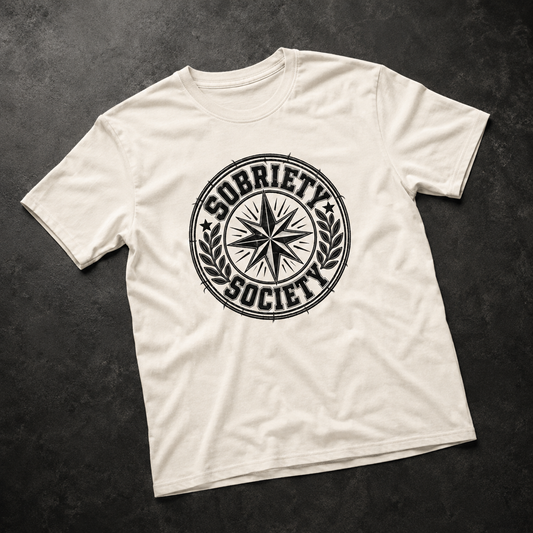 An off-white crewneck t-shirt with a black distressed circular 'Sobriety Society' graphic on the chest, laid flat on a dark textured background.