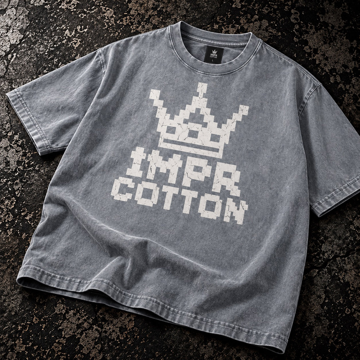 A washed gray short-sleeve t-shirt with a white pixelated crown and 'IMPR COTTON' graphic, laid flat on a dark textured background.