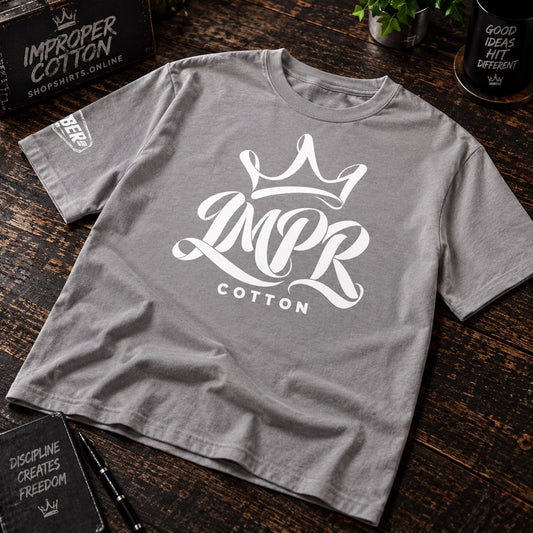 IMPR crown logo on a light gray crew neck tee laying on a dark wooden table slightly at an angle 