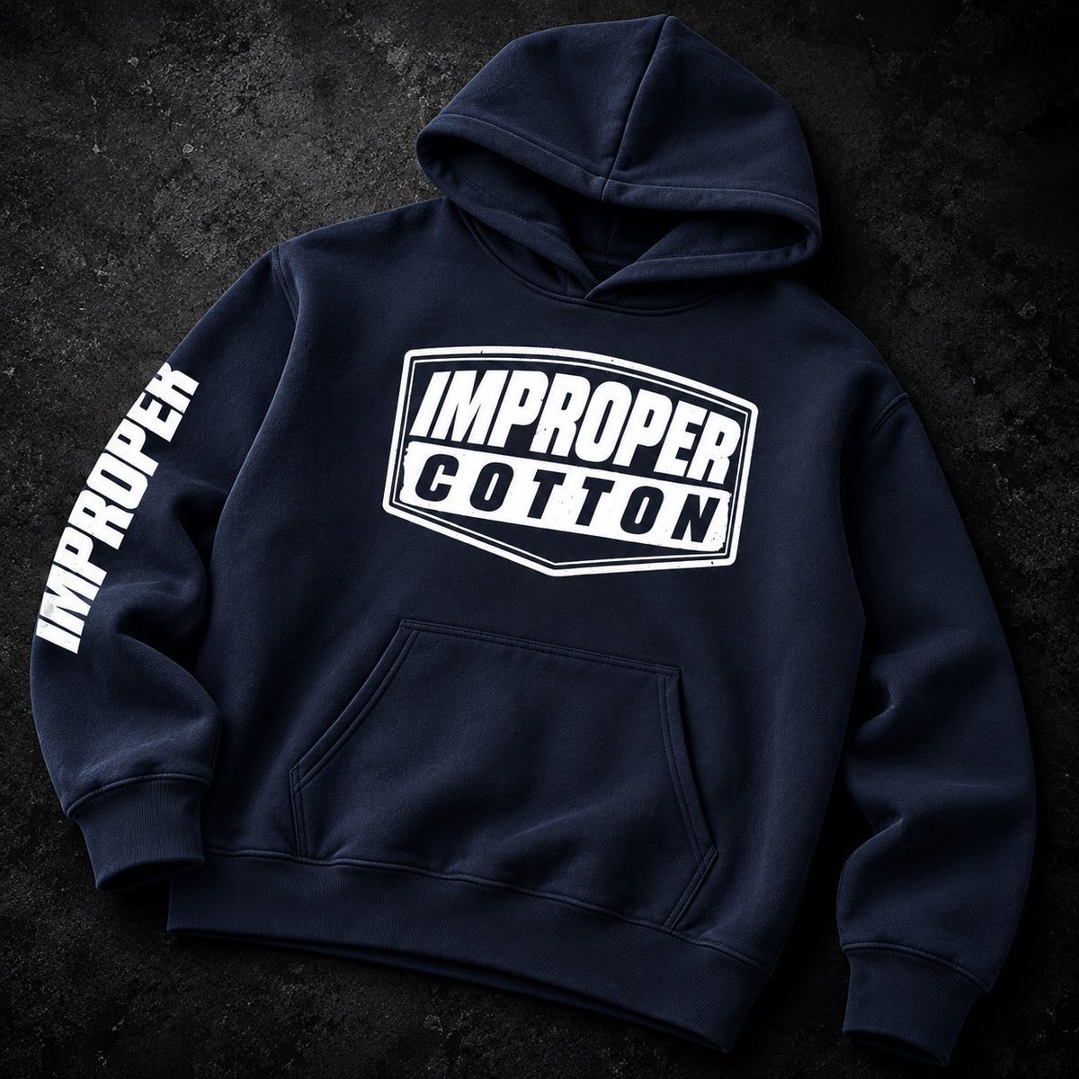 A navy blue pullover hoodie laid flat on a dark textured background. The hoodie features a large white graphic on the chest reading 'IMPROPER COTTON' and 'IMPROPER' printed vertically in white along the left sleeve.
