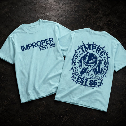 Two light blue t-shirts displayed flat on a dark textured background, showing both the front and back designs. The front features the text 'IMPROPER EST 86' in dark blue.