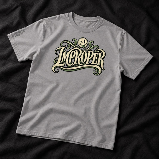 A light gray crewneck t-shirt featuring a stylized graphic print of the word 'IMPROPER' in cream-colored gothic lettering with green flourishes and a skull motif, laid flat on a dark textured fabric background.