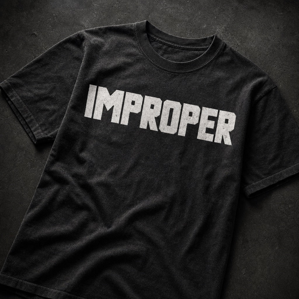 A black short-sleeve t-shirt with the word 'IMPROPER' printed across the chest in distressed white block letters, laid flat on a dark textured background.