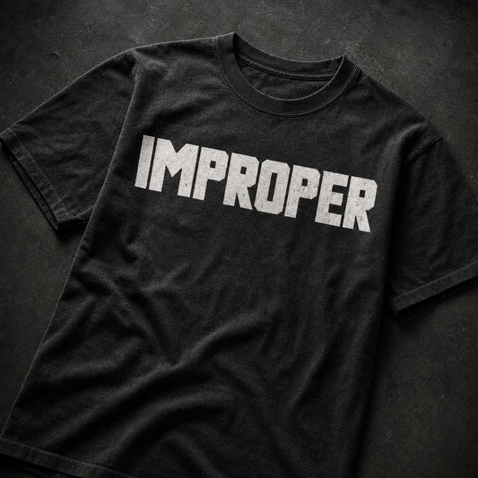 A black short-sleeve t-shirt with the word 'IMPROPER' printed across the chest in distressed white block letters, laid flat on a dark textured background.