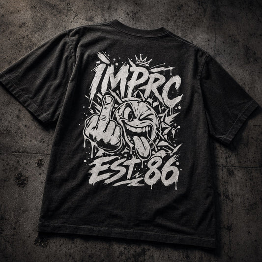 A black graphic t-shirt laid flat on a textured dark gray concrete background. The back of the shirt features a large white spray-paint style graphic with the text 'IMPRC EST.