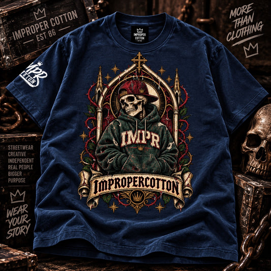 A navy blue short-sleeve graphic T-shirt laid flat on a rustic dark wood background. The shirt features a large front print of a skeleton wearing a red cap and green hoodie with the text 'IMPR' and 'Improperrcotton,' plus ornate red and gold decorative elements.
