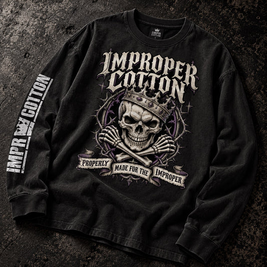 A black long-sleeve graphic t-shirt laid flat on a dark textured background. The shirt features a large front graphic of a skull wearing a crown with crossed bones underneath, the words 'IMPROPER COTTON' in a gothic font above, and 'PROPERLY MADE FOR THE IMPROPER' on a banner below.