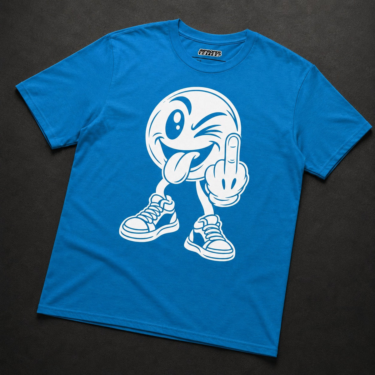 A bright blue short-sleeve t-shirt with a white graphic of a winking cartoon character sticking out its tongue and making a middle finger gesture, laid flat on a dark textured background.