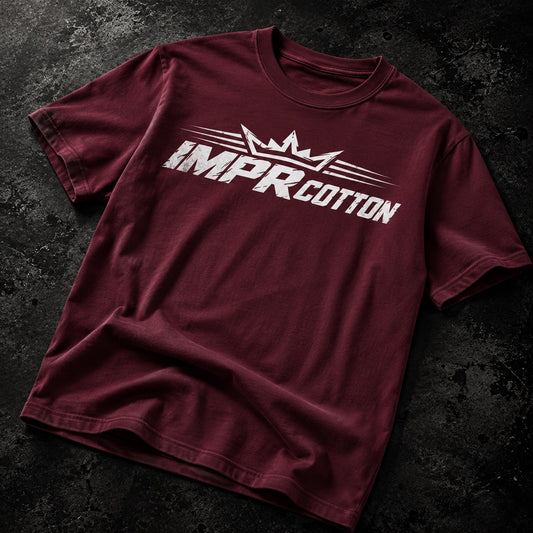 A maroon short-sleeve t-shirt with a white 'IMPR COTTON' graphic and crown logo printed across the chest, laid flat on a dark textured background.