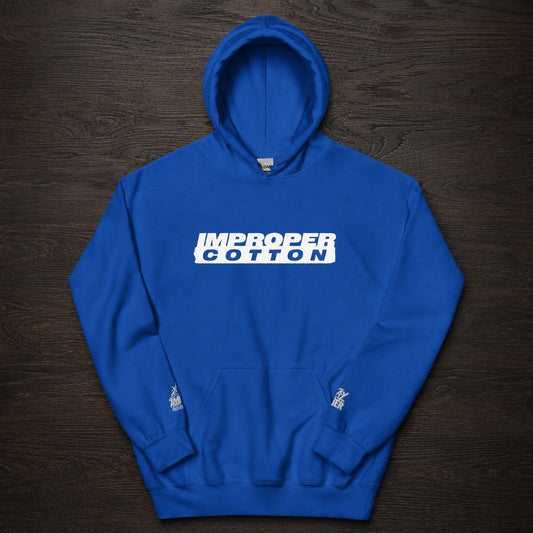 A royal blue pullover hoodie with a white graphic text print reading 'IMPROPER COTTON' across the chest, laid flat on a dark wood background.