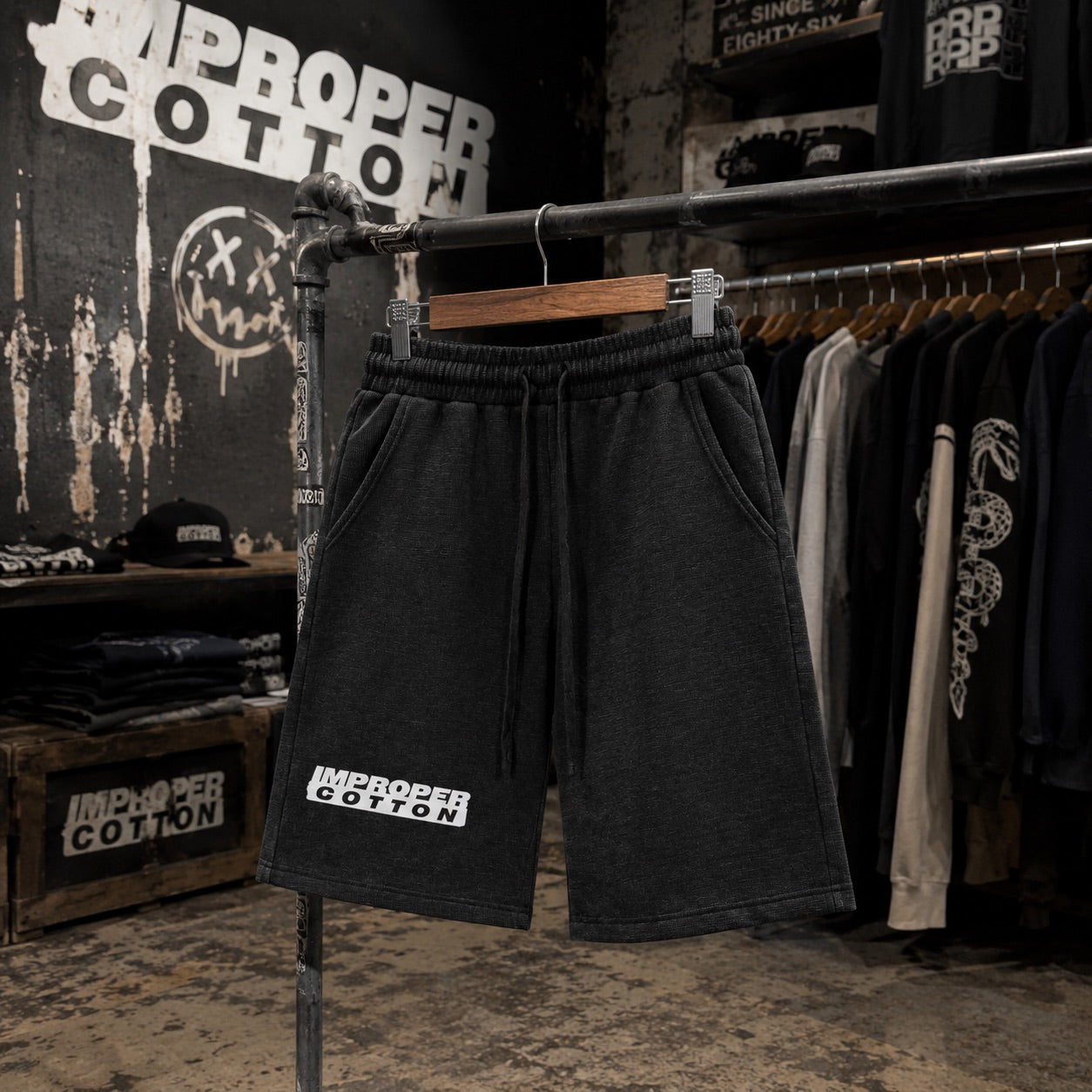 Black sweat shorts with a white 'IMPROPER COTTON' logo on the left leg, hanging on a clothing rack in a retail store setting.