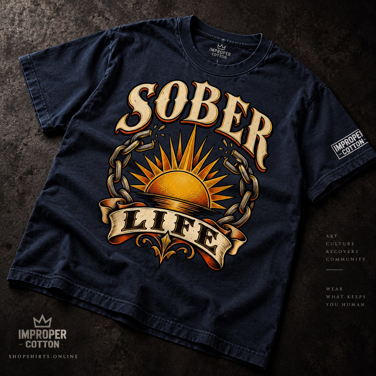 Navy Improper Cotton Sober Life vintage-wash T-shirt featuring a golden sunrise surrounded by broken chains, laid slightly angled on a dark textured background with ShopShirts.online branding.