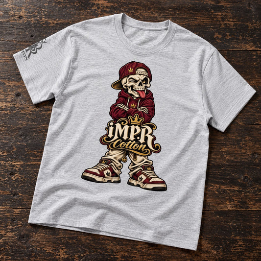 A heather gray short-sleeve t-shirt with a detailed graphic of a cartoon skeleton wearing a maroon hoodie, gold cap, and sneakers, with the text 'IMPR Cotton' below. The shirt is laid flat on a dark wood background.