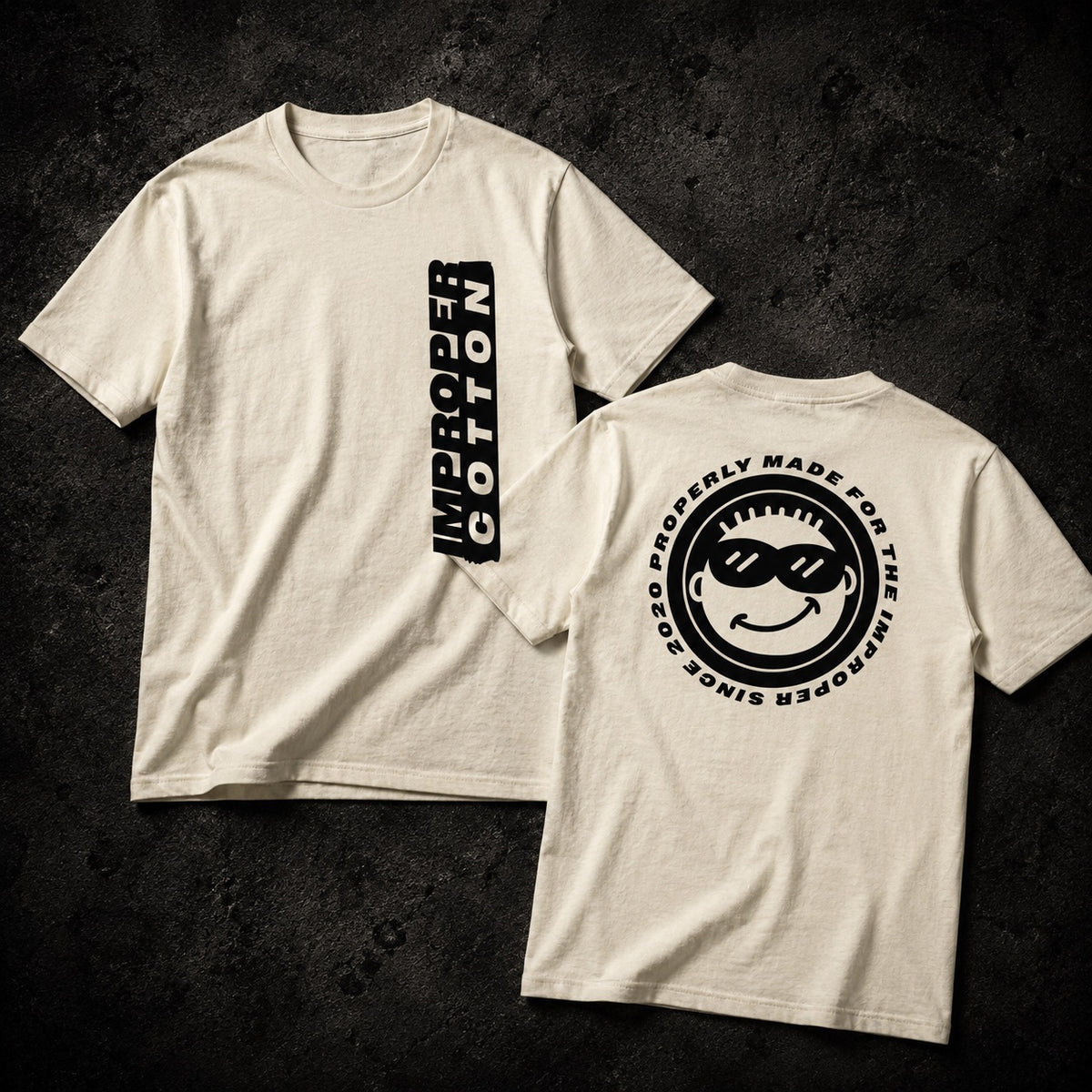 Two off-white short-sleeve t-shirts shown on a dark textured background, displaying the front and back designs. The front features a vertical black graphic reading 'IMPROPER COTTON'.