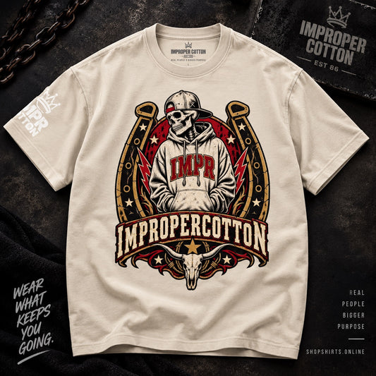 A cream-colored t-shirt featuring a large graphic print of a skull in a cowboy hat inside a horseshoe with the text 'IMPR' and 'IMPROPERCOTTON'. The shirt is laid flat on a dark textured background with decorative chain and text overlays.