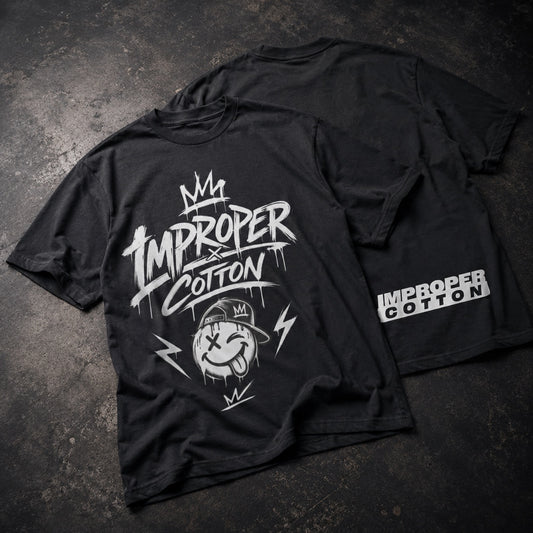 Two black short-sleeve graphic T-shirts laid flat on a dark textured surface, showing the front and back designs. The front features a large white 'IMPROPER x COTTON' graphic with a cartoon face and lightning accents, and the back shows a smaller matching 'IMPROPER x COTTON' print near the lower right side.