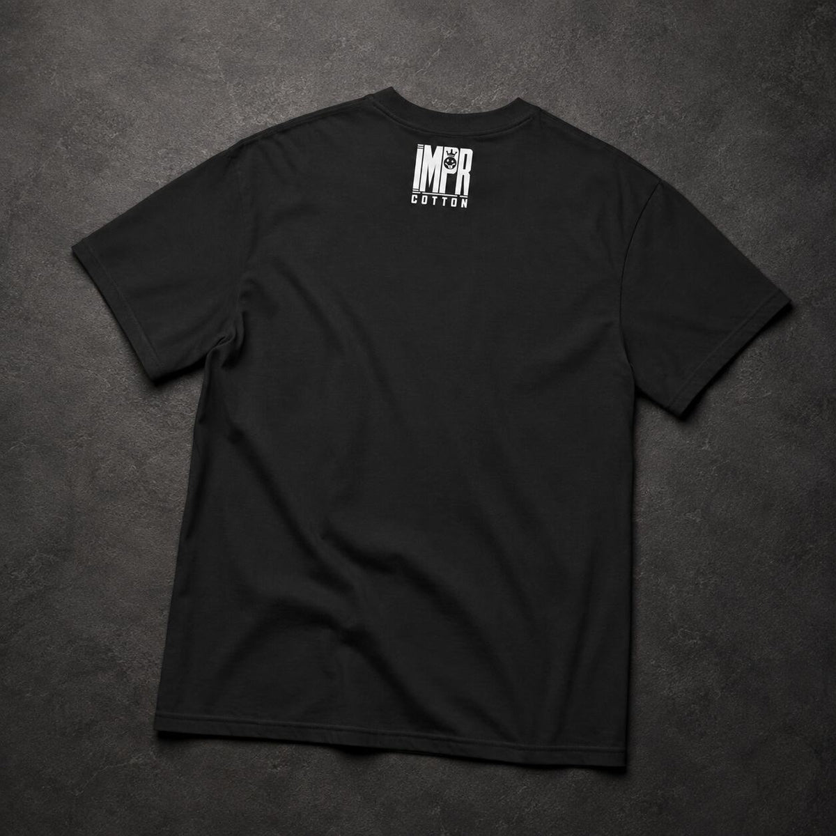 A black short-sleeve t-shirt laid flat on a dark textured background, featuring a white vertical graphic print on the upper back that reads 'IMPR' above 'COTTON'.
