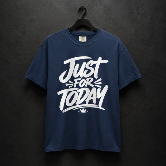 A navy blue short-sleeve t-shirt hanging on a black hanger against a dark textured wall. The shirt features a large white graphic print on the front that reads 'Just For Today' with a small crown logo underneath.