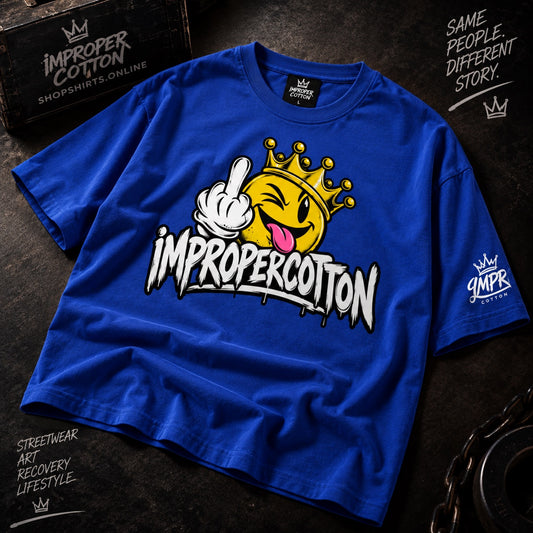A bright blue graphic T-shirt laid flat on a dark textured surface. The shirt features a large front graphic of a yellow crown emoji face giving the middle finger, with the text 'IMPROPERCOTTON' in white graffiti-style lettering.