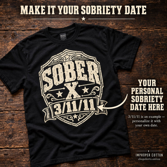 A black short-sleeve graphic T-shirt laid flat on a rustic wooden background, with a large cream shield-style print reading 'Sober X 3/11/11.' Text overlays explain that the date can be customized, and the bottom-right corner shows the Improper Cotton brand.