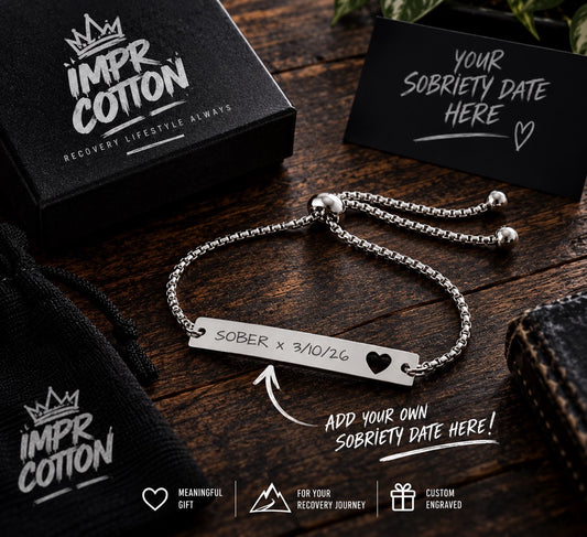 A silver adjustable bracelet with a rectangular bar engraved with 'SOBER x 3/10/26' and a heart icon, displayed on a dark wooden surface with a black gift box, branded black pouch, and a card reading 'YOUR SOBRIETY DATE HERE'.