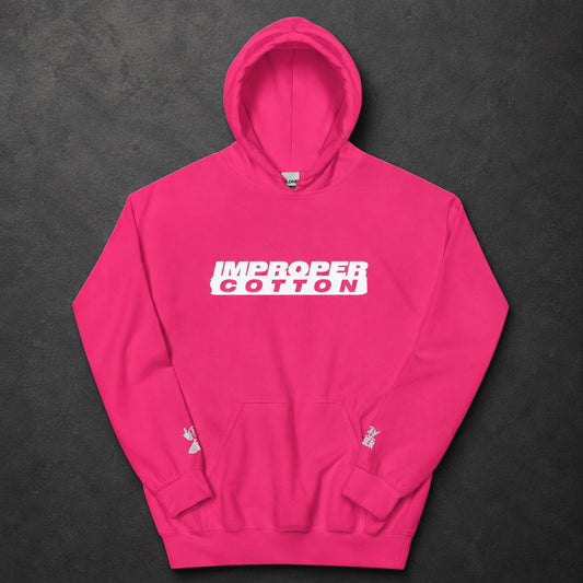 A bright pink pullover hoodie laid flat on a dark textured background. The chest features a white rectangular graphic with the words 'IMPROPER COTTON' in white.