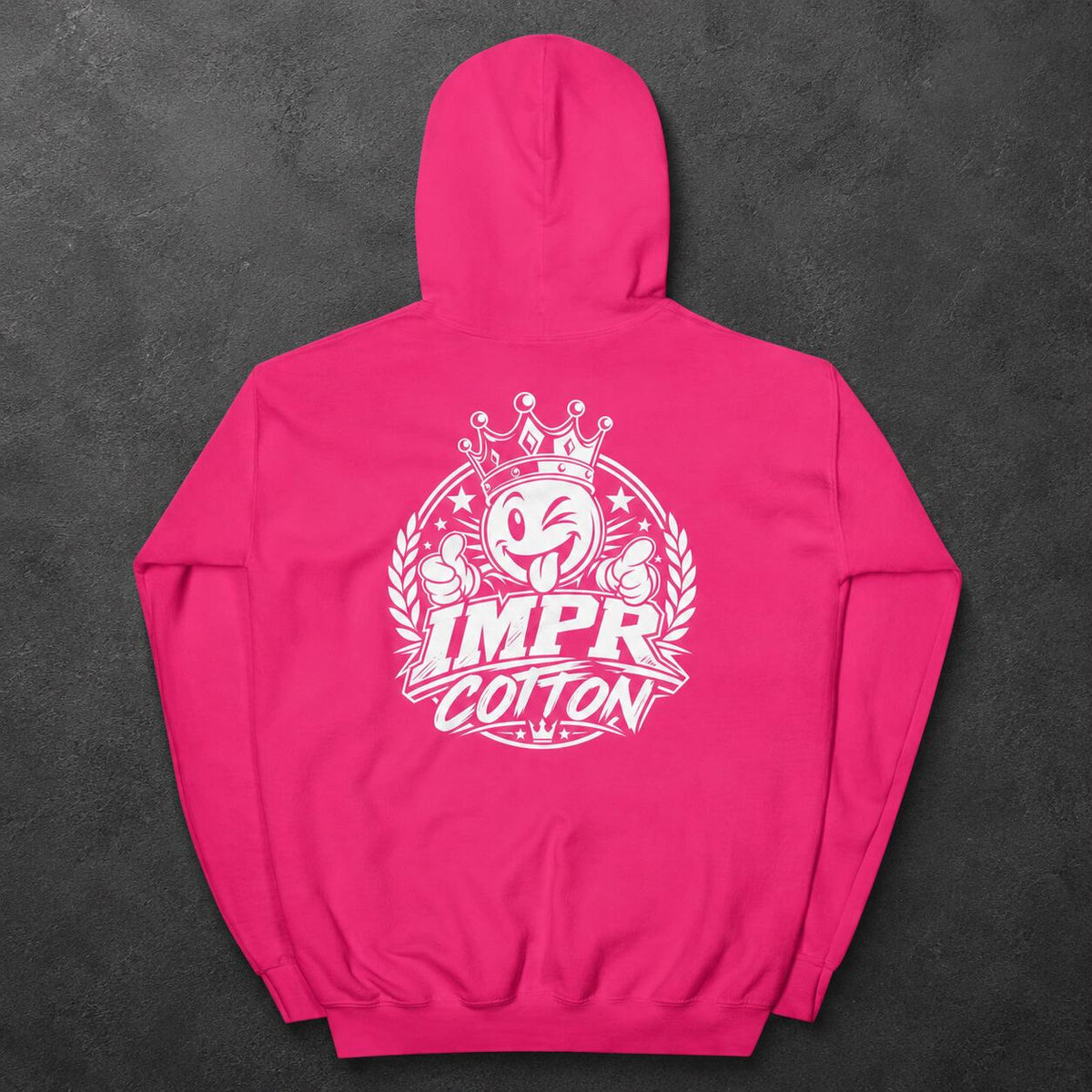 A bright pink hoodie shown from the back, featuring a large white graphic print with a cartoon face, crown, laurel wreath, and the words “IMPR COTTON.” The hoodie is laid flat on a dark textured background.