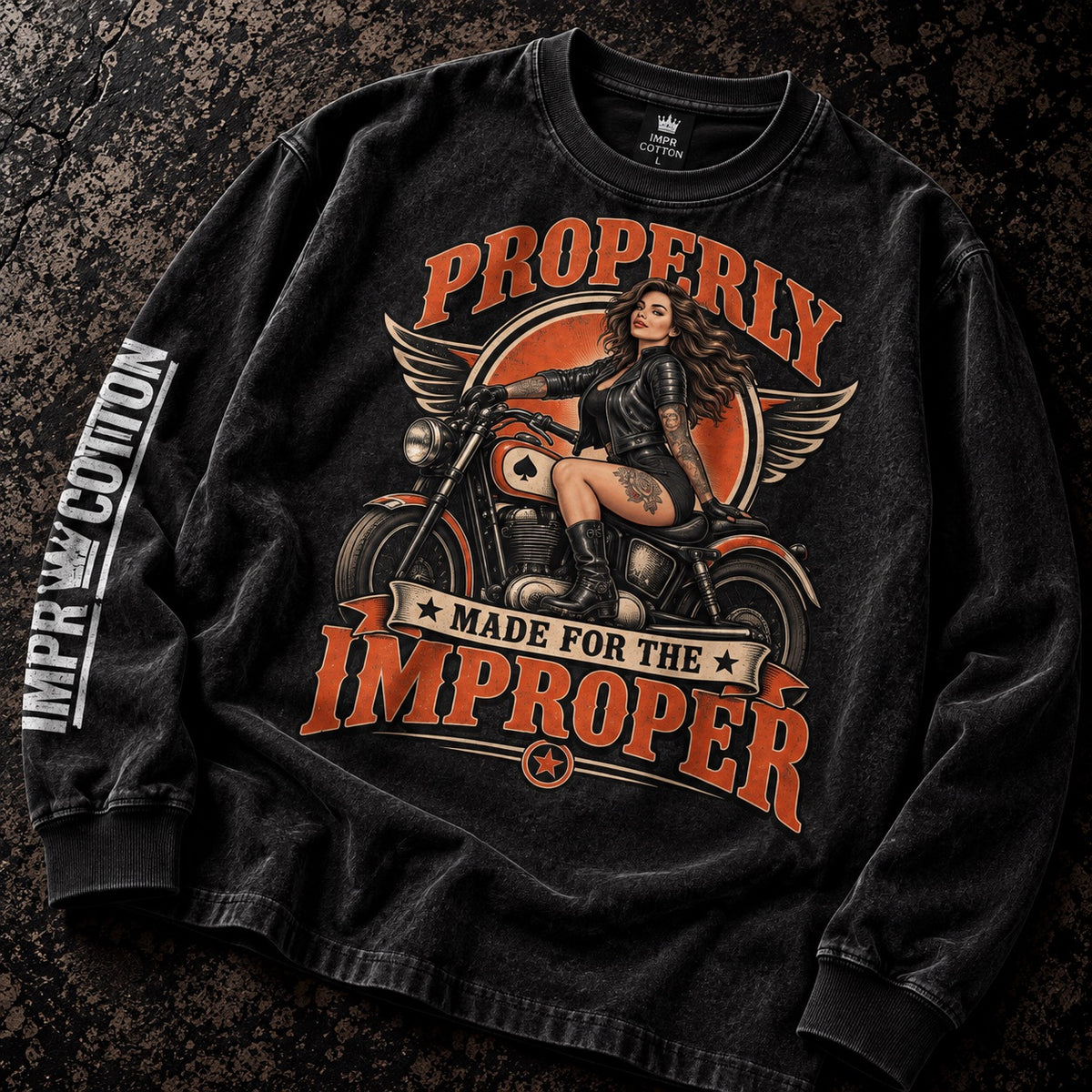 A black long-sleeve t-shirt with a vintage-style biker graphic, laid flat on a dark textured background. The graphic features a woman on a motorcycle with the text 'PROPERLY MADE FOR THE IMPROPER' in orange.