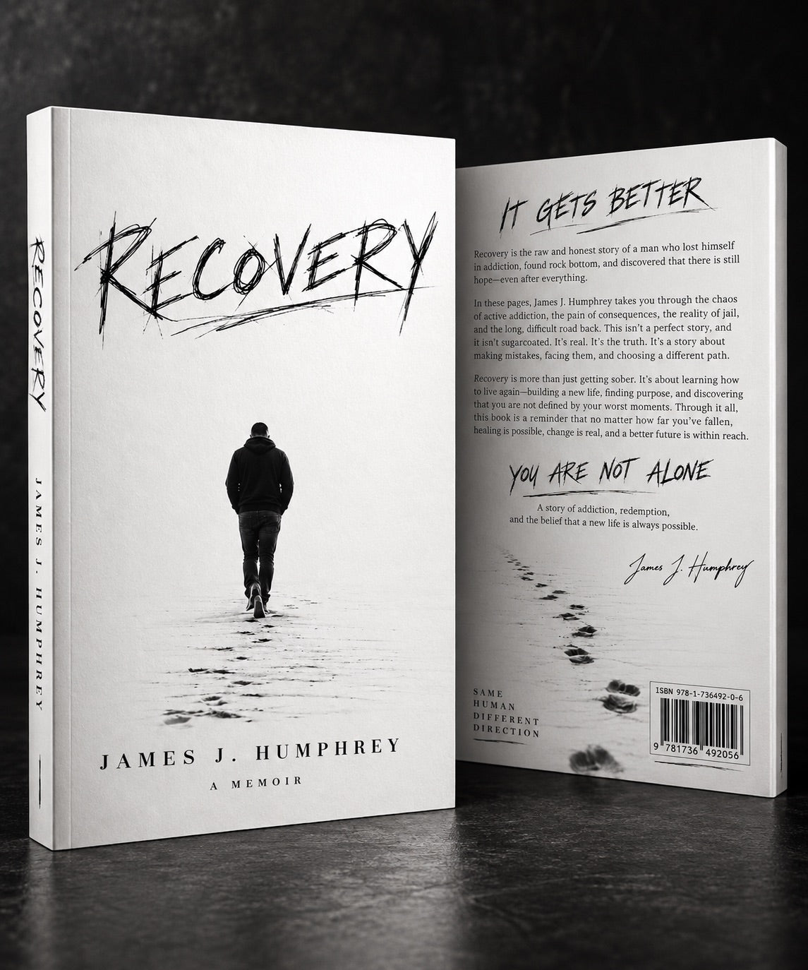 Stack of Recovery A Memoir by James J. Humphrey books on a dark wooden table with one copy standing upright, featuring the minimalist black-and-white cover and Improper Cotton branding.