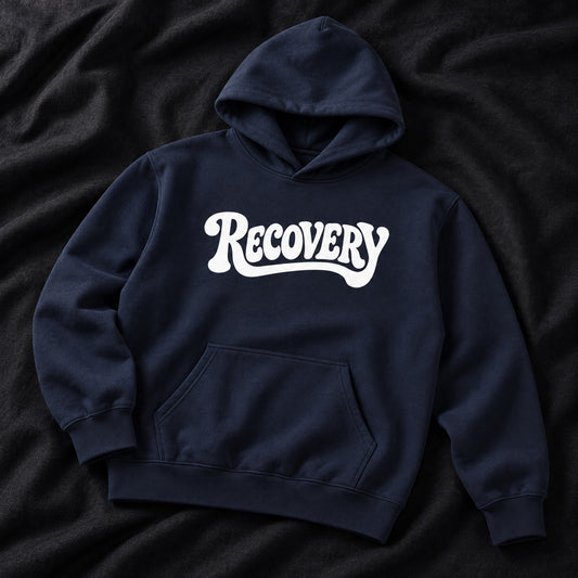 A navy blue pullover hoodie with the word 'RECOVERY' printed in white across the chest, laid flat on a dark textured fabric background.