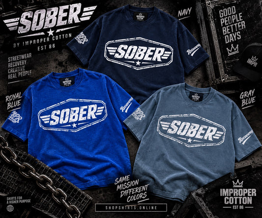 Three short-sleeve crew-neck t-shirts displayed together in different colors: navy, royal blue, and heather gray. Each shirt features a large distressed white 'SOBER' logo across the chest with wing and star details.