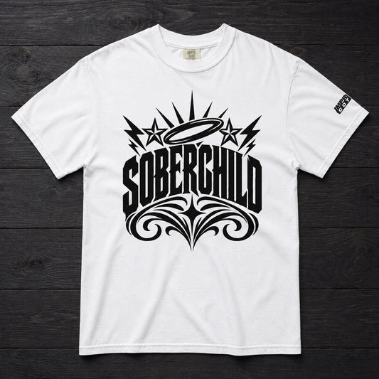 A white short-sleeve crewneck t-shirt with a large black graphic on the front reading 'SOBERCHILD' in stylized lettering, featuring stars, lightning bolts, and ornate flourishes. The shirt is laid flat on a dark wood plank background.