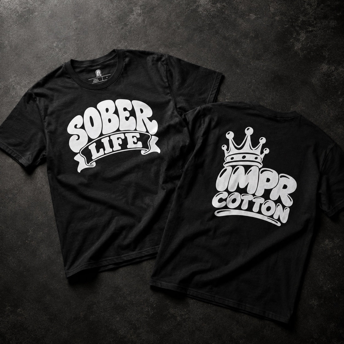 Two black short-sleeve T-shirts laid flat on a dark textured surface, showing the front and back designs. The front shirt has a white graphic reading “SOBER LIFE,” and the back shirt has a white graphic with a crown above stylized text that appears to read “IMPR” and “COTTON.