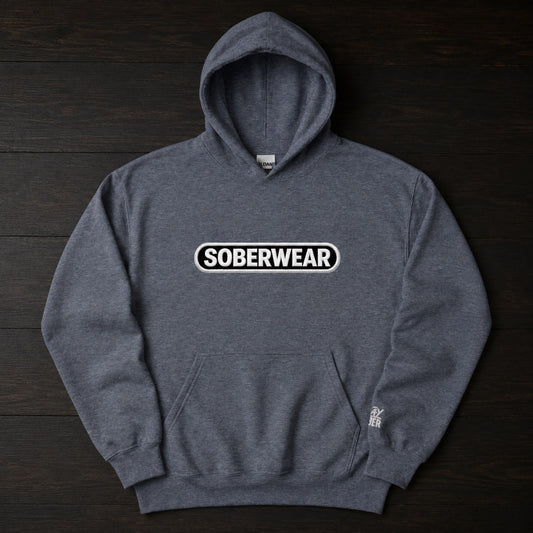 A dark heather gray pullover hoodie with a white and black 'SOBERWEAR' logo on the chest, laid flat on a dark wood background.