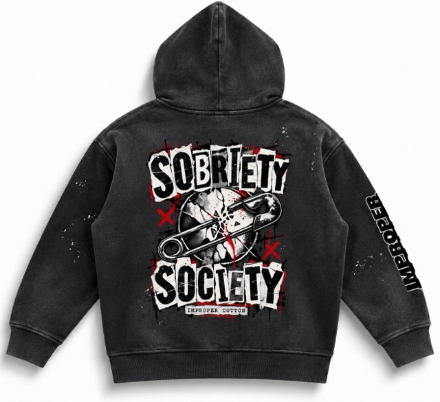 A black washed hooded sweatshirt shown from the back, featuring a large graphic print with the words 'Sobriety Society' in distressed white lettering, red splatter accents, a safety pin over a mugshot-style image, and 'Life is Hard' printed down one sleeve.