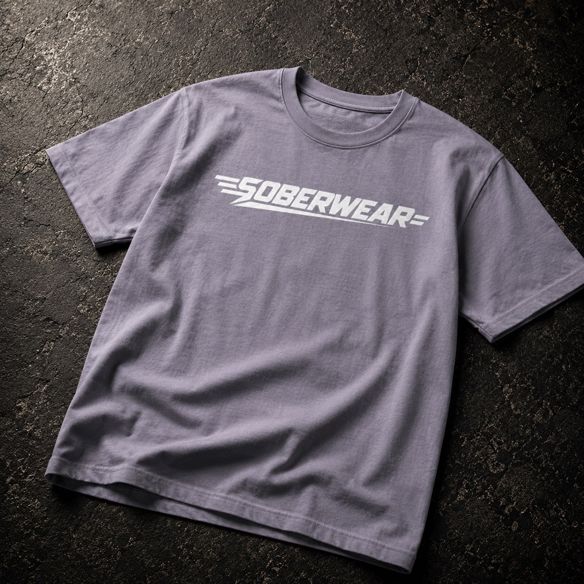 A heather gray crewneck t-shirt with a white 'SOBERWEAR' logo printed across the chest, laid flat on a dark textured asphalt surface.