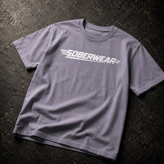 A heather gray crewneck t-shirt with a white 'SOBERWEAR' logo printed across the chest, laid flat on a dark textured asphalt surface.